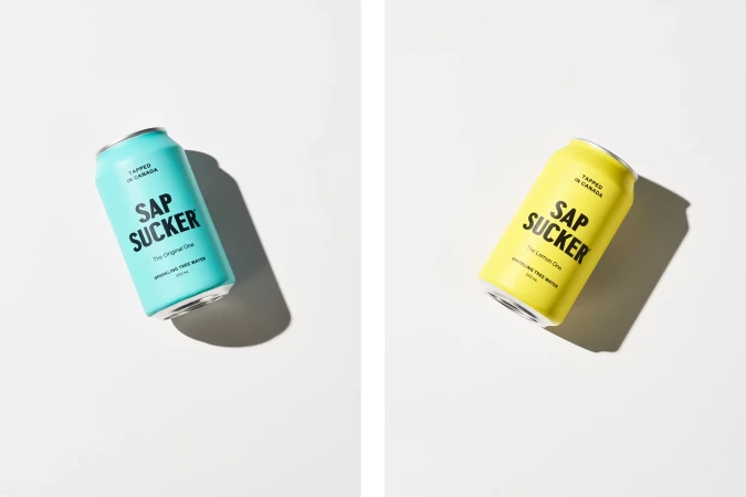 Two cans of Sap Sucker sparkling tree water, one yellow and one aqua blue, against a white backdrop with defined shadows. Food and beverage.