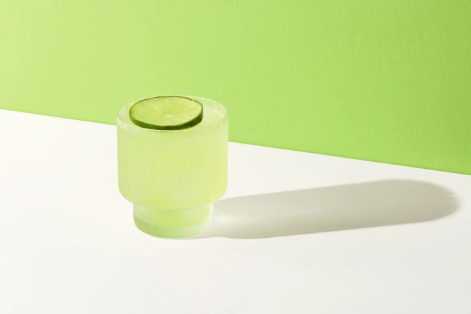 Refreshing light green cocktail in clear glass with lime slice garnish, set against a two-tone green and white backdrop.