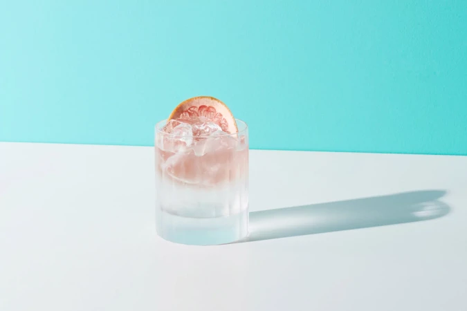 Refreshing grapefruit cocktail with ice cubes on a white surface and a turquoise background, offering a cool and crisp beverage concept.