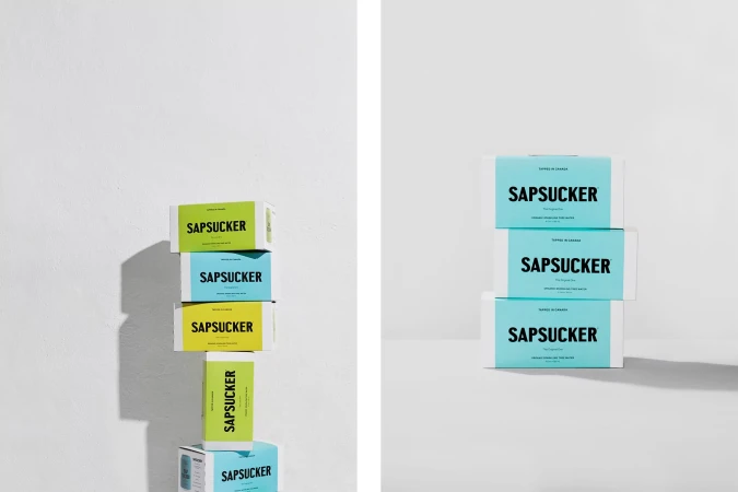 Stacked Sapsucker brand cartons in green and aqua, contrasting against a white background and casting soft shadows in the studio.