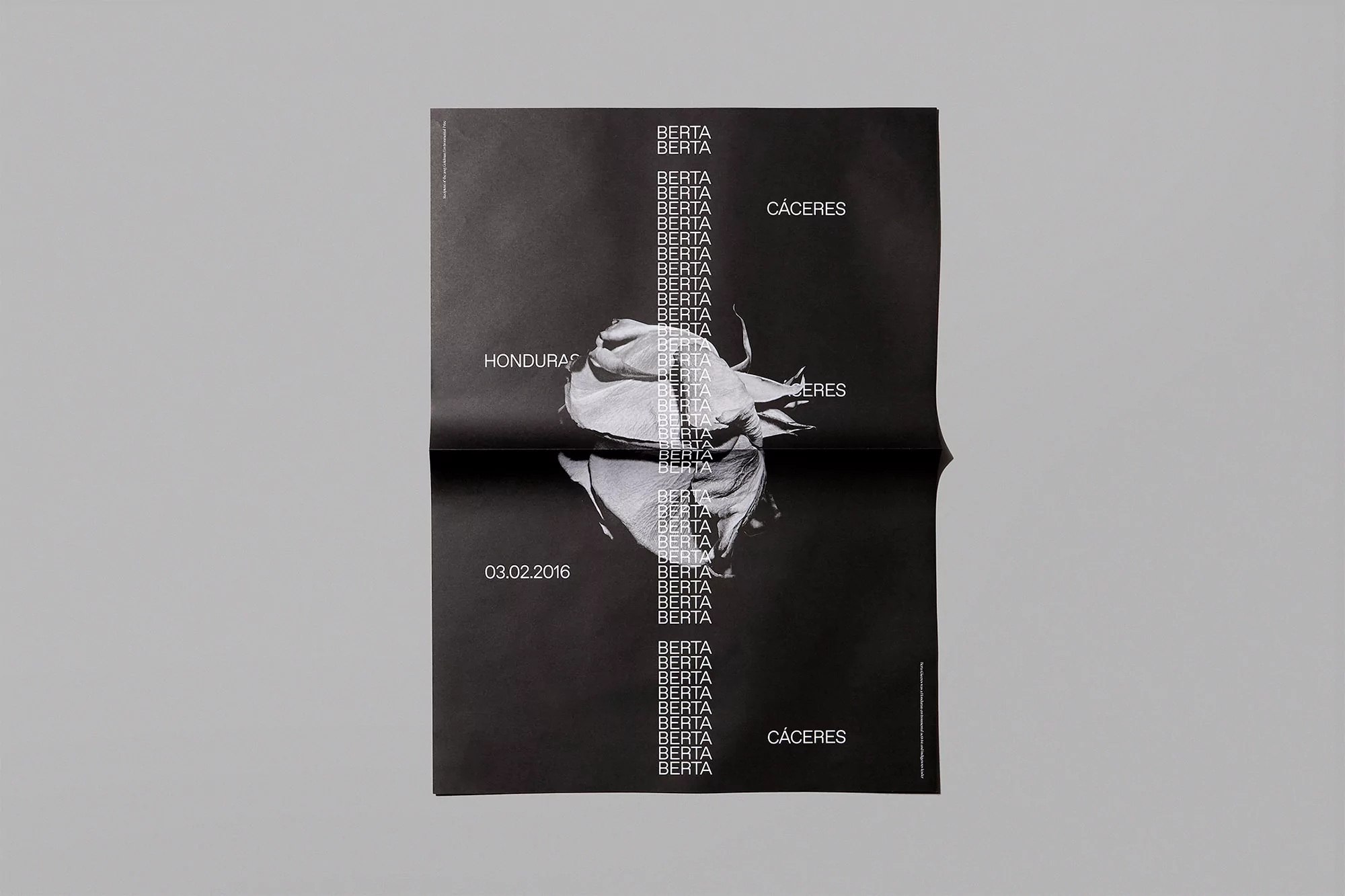 Black poster features a white flower, text repetitions, and Honduras/Cáceres locations. The poster is photographed on a gray surface.