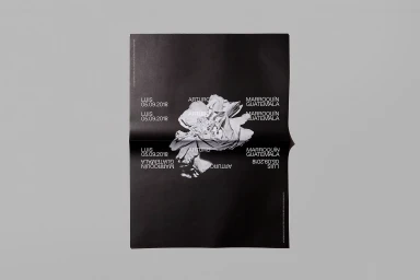 Black folded paper poster featuring white typographic layout and central floral graphic on a light grey background