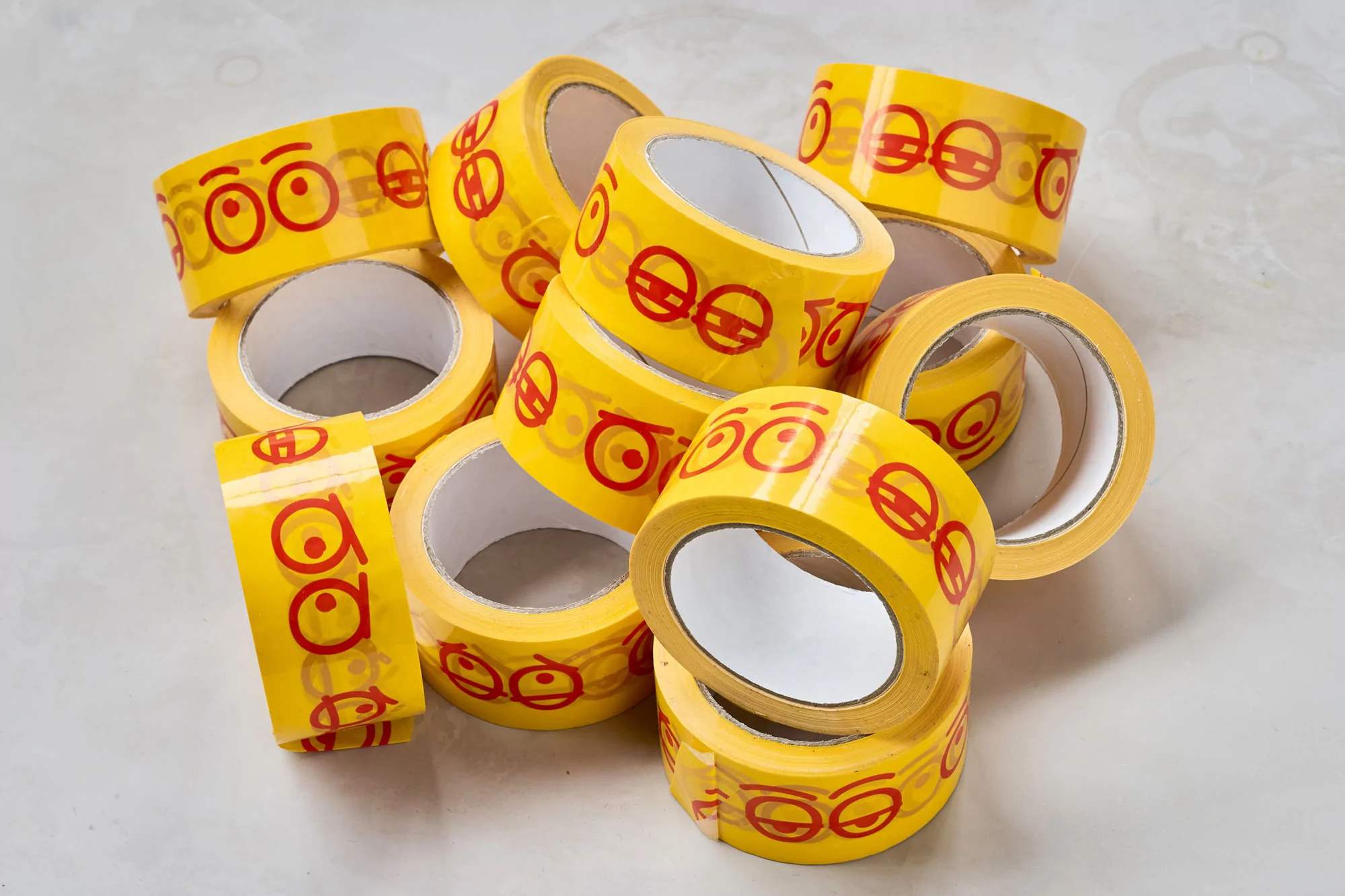 Stack of yellow tape rolls with red circular designs, arranged indoors under bright lighting, showcasing packaging materials.