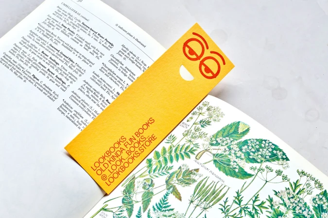 Botanical book open with yellow bookmark featuring a smiley face; educational and fun reading promotion.