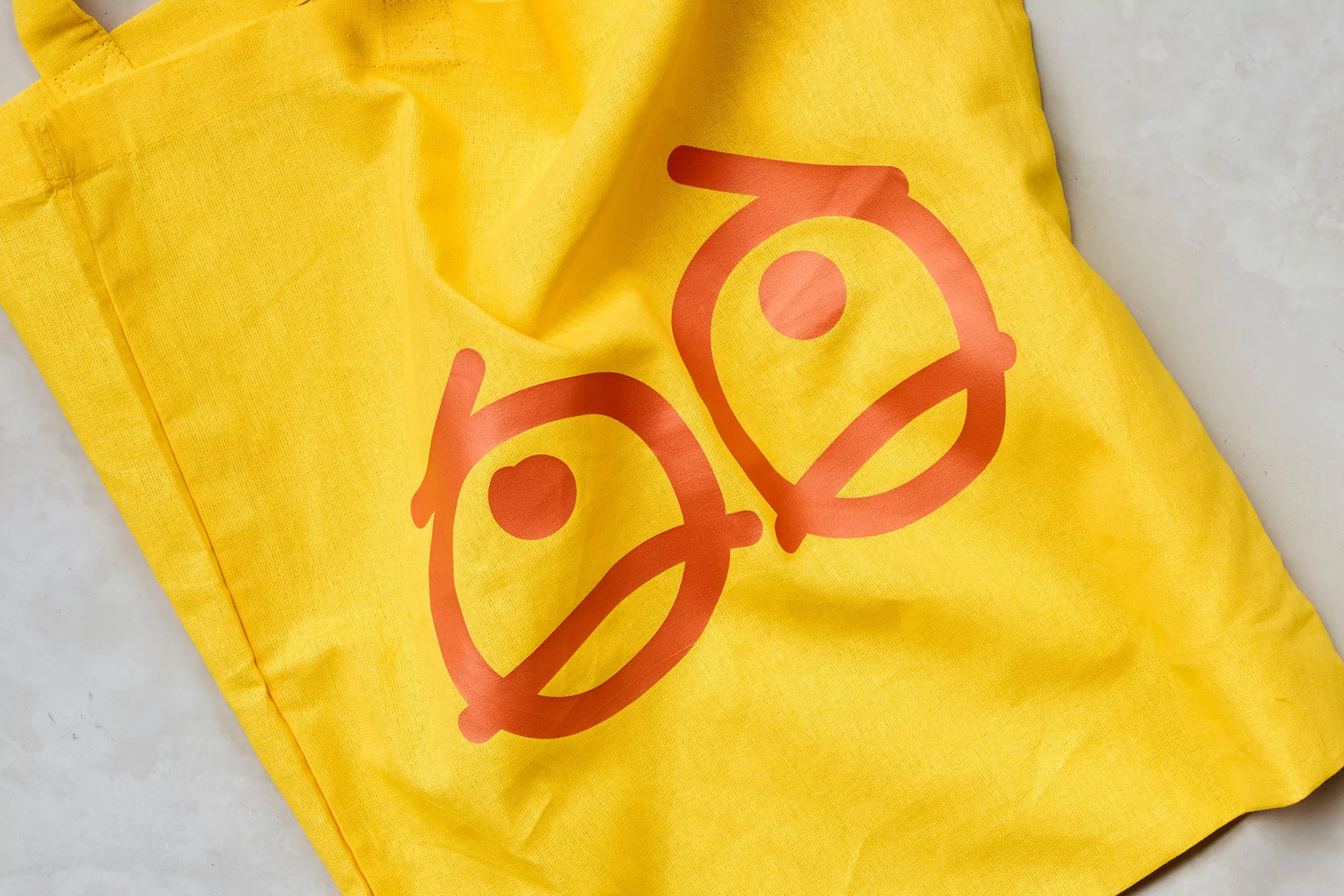 Close-up of a bright yellow tote bag with an orange graphic design printed on it, creating a visually striking and cheerful image.