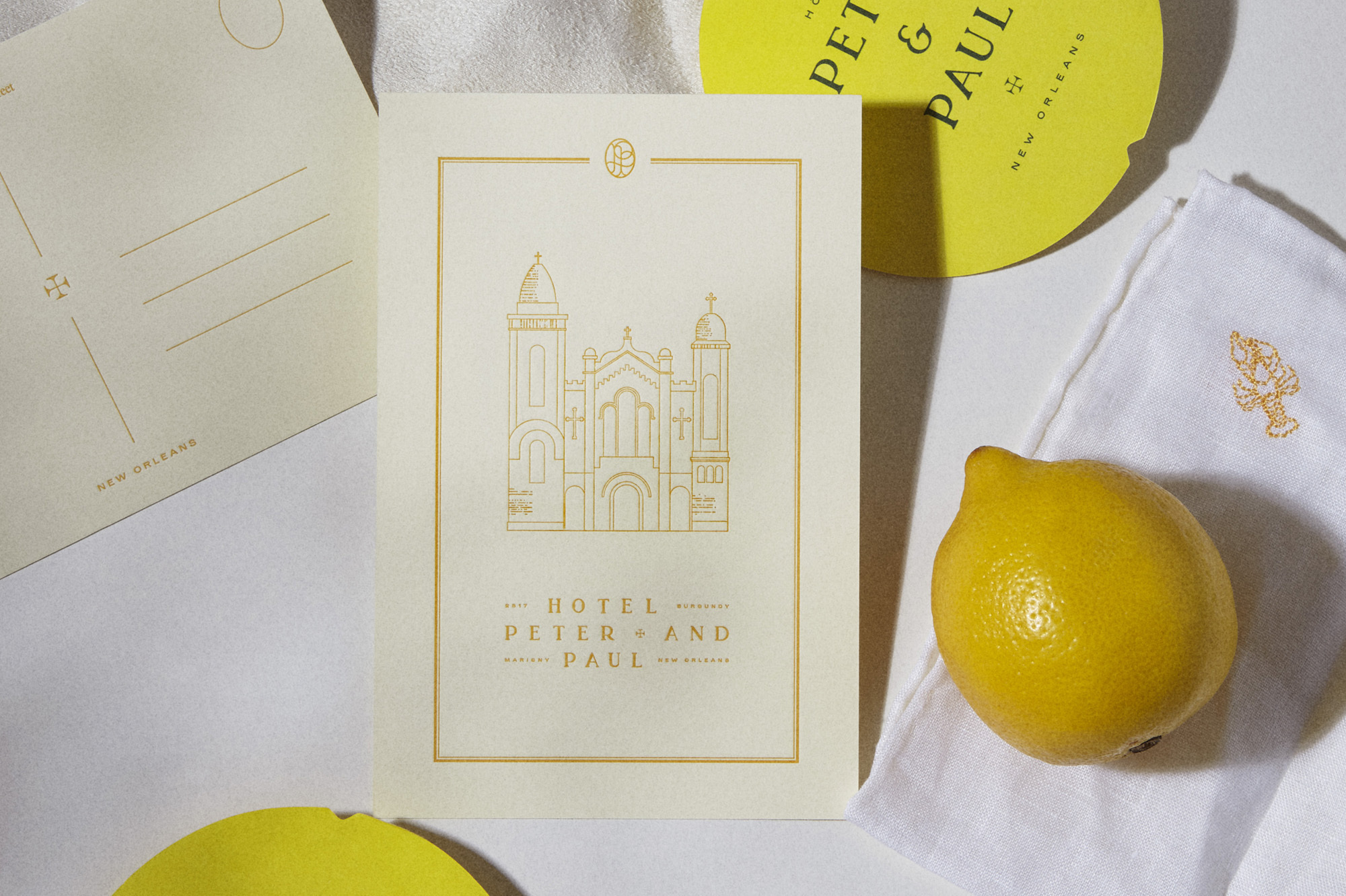 Close-up of stationery featuring an illustration of Hotel Peter and Paul in New Orleans, a round yellow coaster, lemon, and white cloth.
