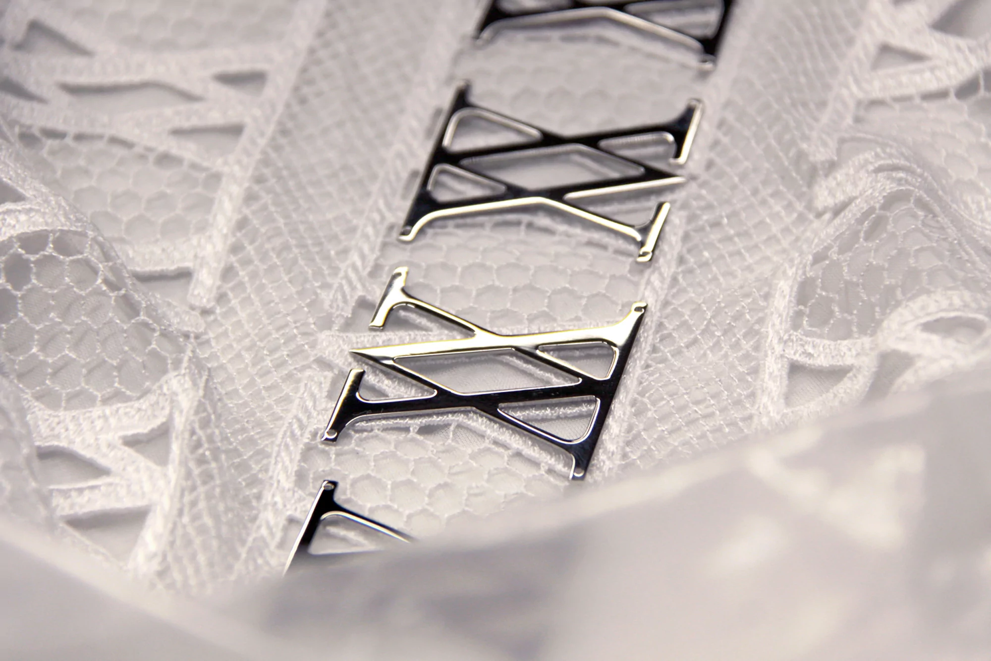 Close-up of a white lace fabric with decorative metal letter 'T' appliques, creating a textured and patterned textile detail.