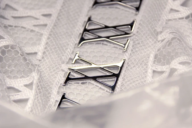 Close-up of a white lace fabric with decorative metal letter 'T' appliques, creating a textured and patterned textile detail.