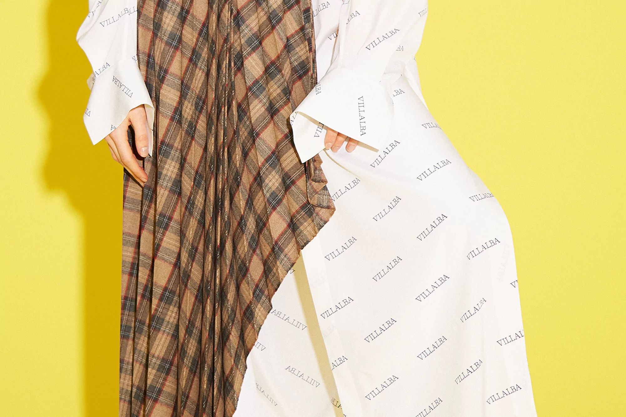 Tan and brown plaid pleated skirt paired with a white shirt printed with black text on a bright yellow background.
