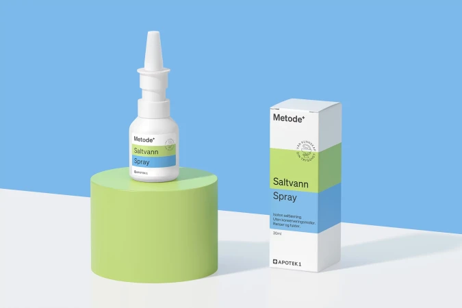 White nasal spray bottle and product box on a green cylindrical stand against a light blue and white background in a studio setting.