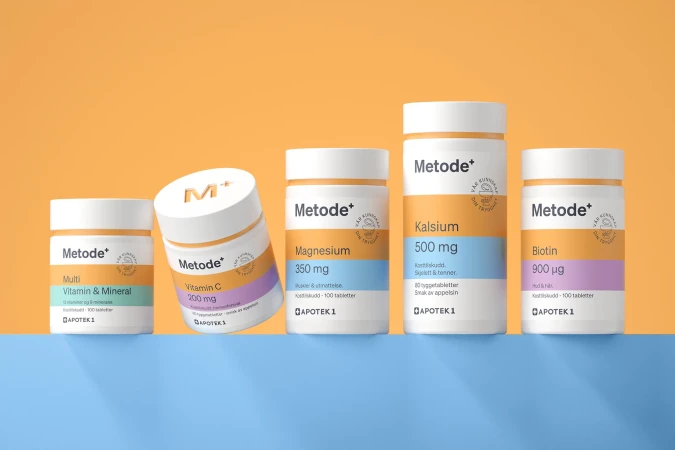 Five bottles of Metode+ vitamins and minerals lined up on a blue surface against an orange background in a studio product shot.