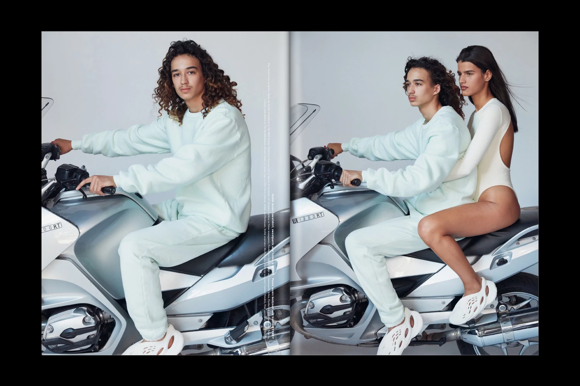 Fashion editorial shot of a young adult male with long curly hair riding a motorcycle with an adult female on a studio background.