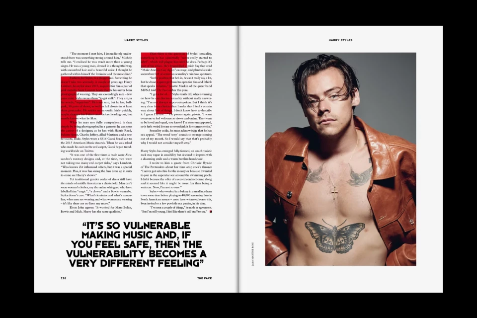 Harry Styles poses shirtless in a magazine layout, wearing a brown leather jacket and a silver cross necklace against a gray backdrop.