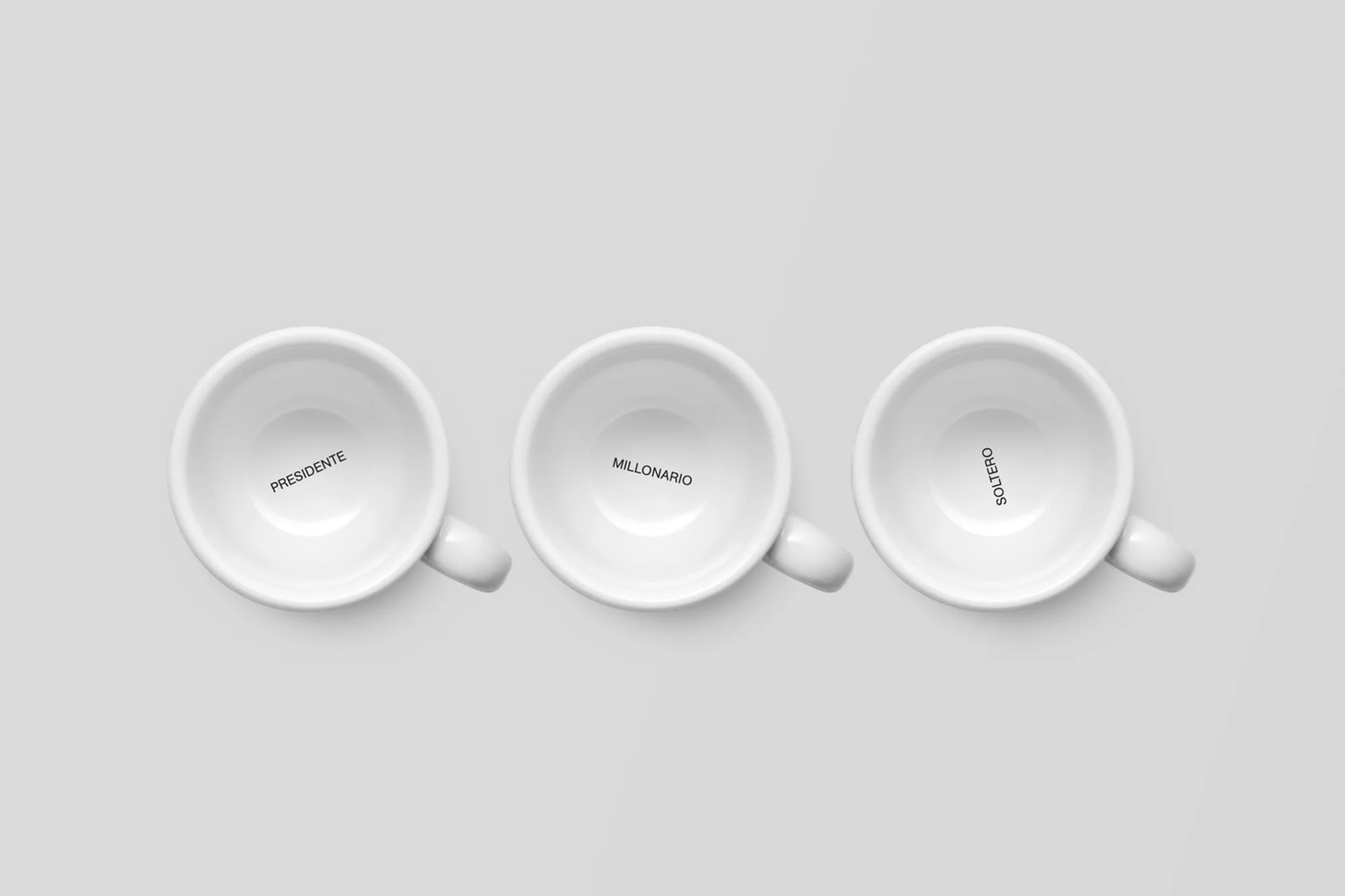 Three white coffee cups with the words 'Presidente,' 'Millonario,' and 'Soltero' printed inside on a neutral background. Minimalist.
