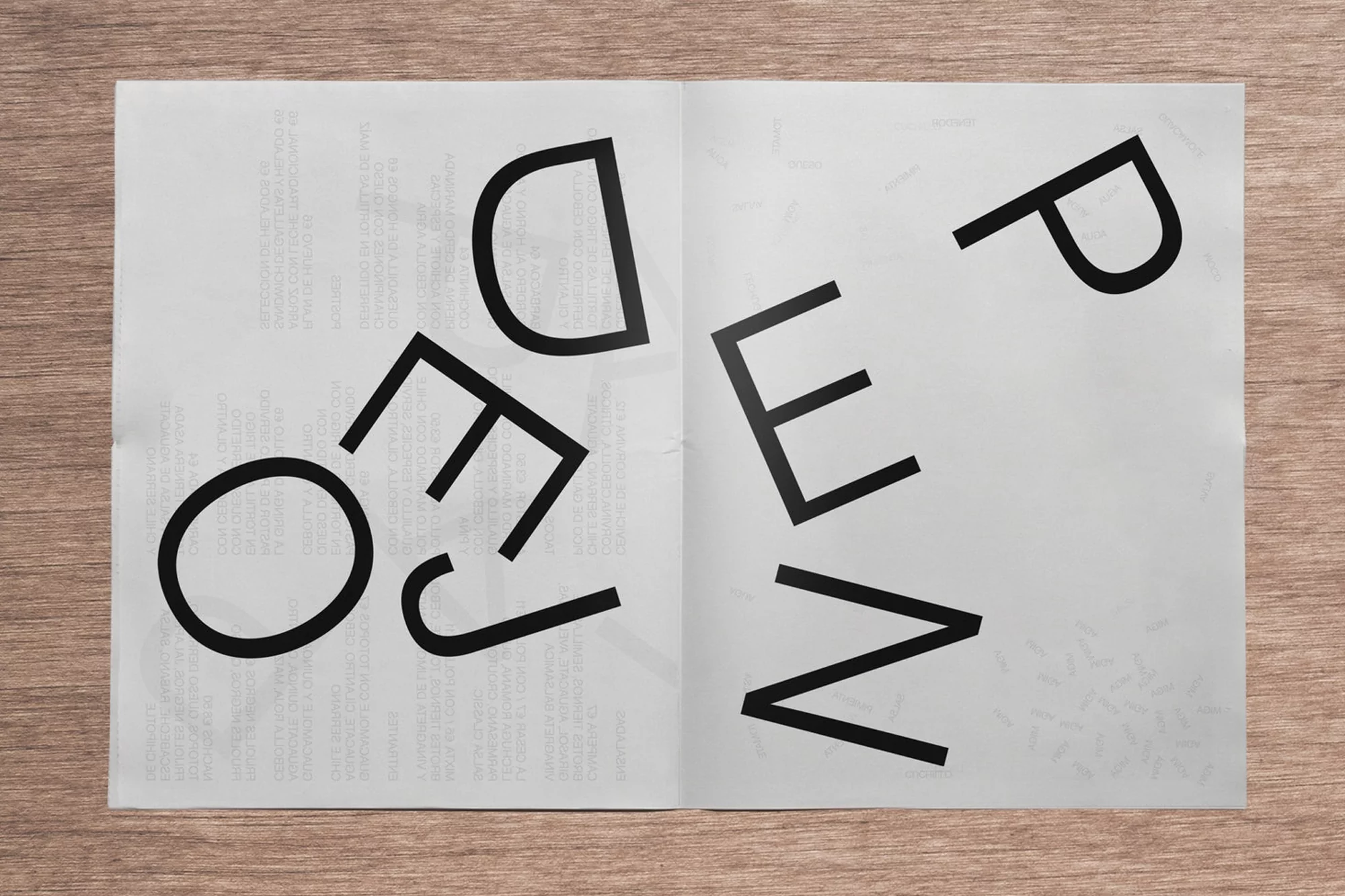 Open magazine spread on wood background. Black text on white paper in large font creates a bold visual design.