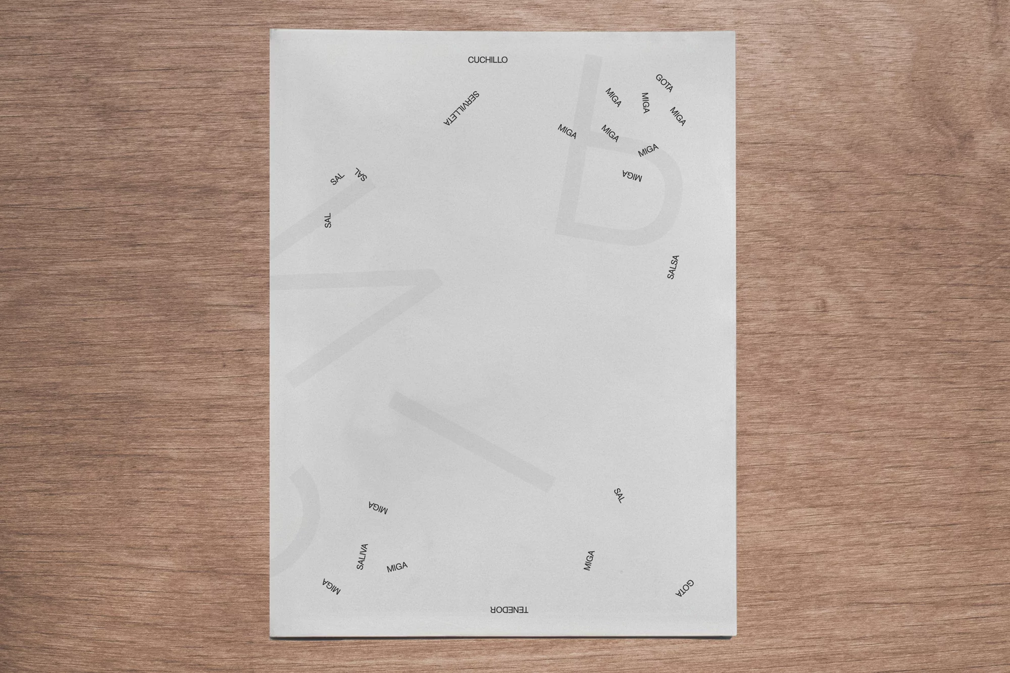Overhead shot of a white page with culinary Spanish words in black text, laid on a wood surface, creating an abstract design.