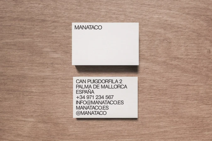 Two white business cards are displayed on a light brown wood table, with contact and company information printed in black ink.