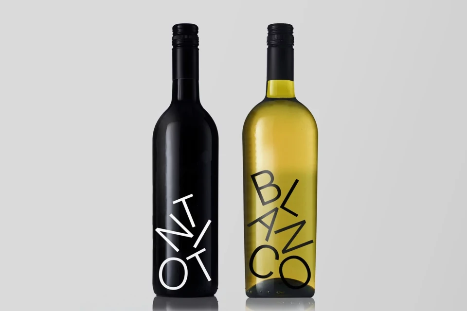 Two wine bottles, one black labeled 'N Tinto', the other clear glass labeled 'Blanco', set against a plain background.