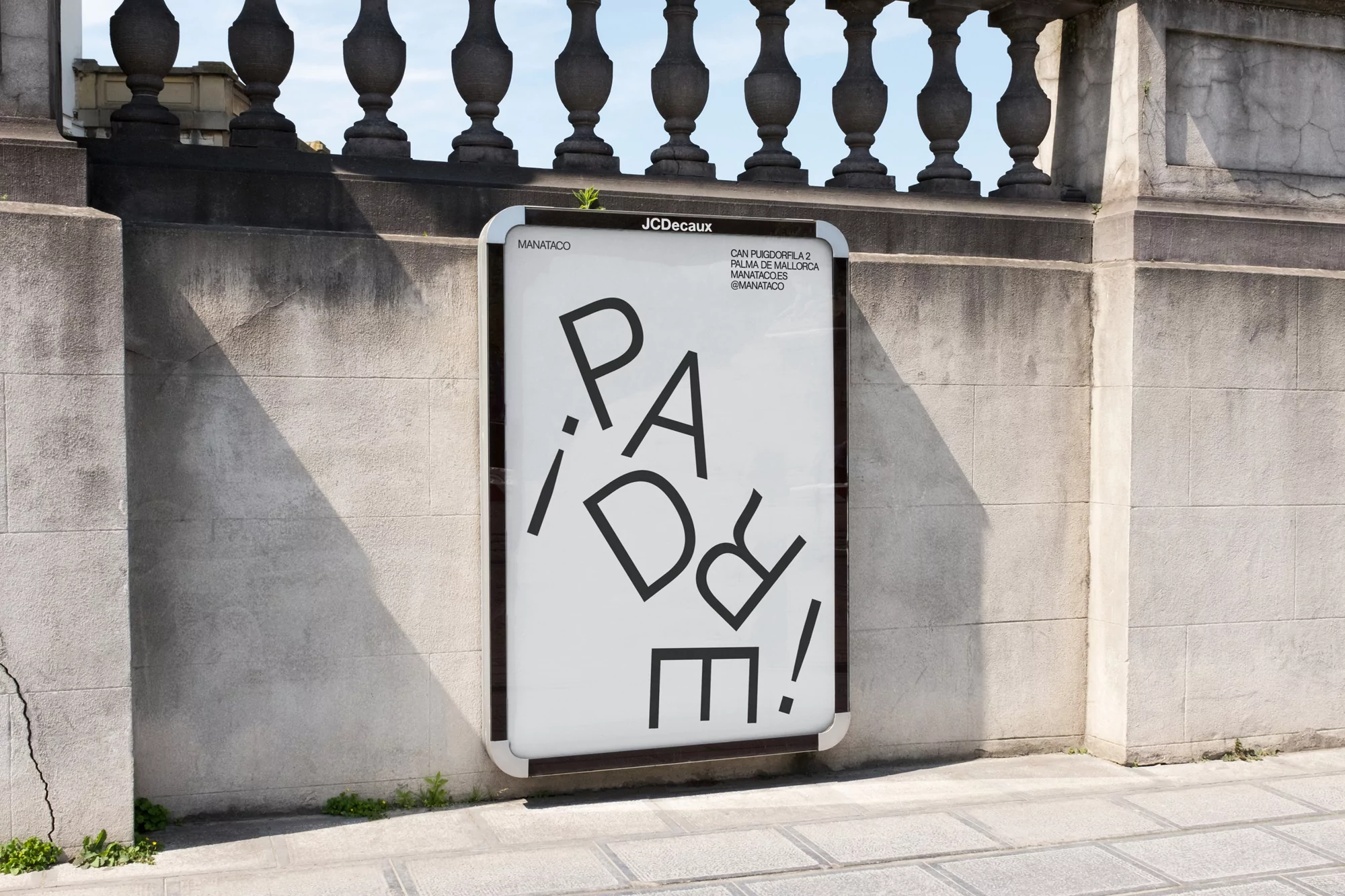 Outdoor advertising billboard featuring black, sans-serif typography on a white background, mounted on a grey stone wall and sidewalk.
