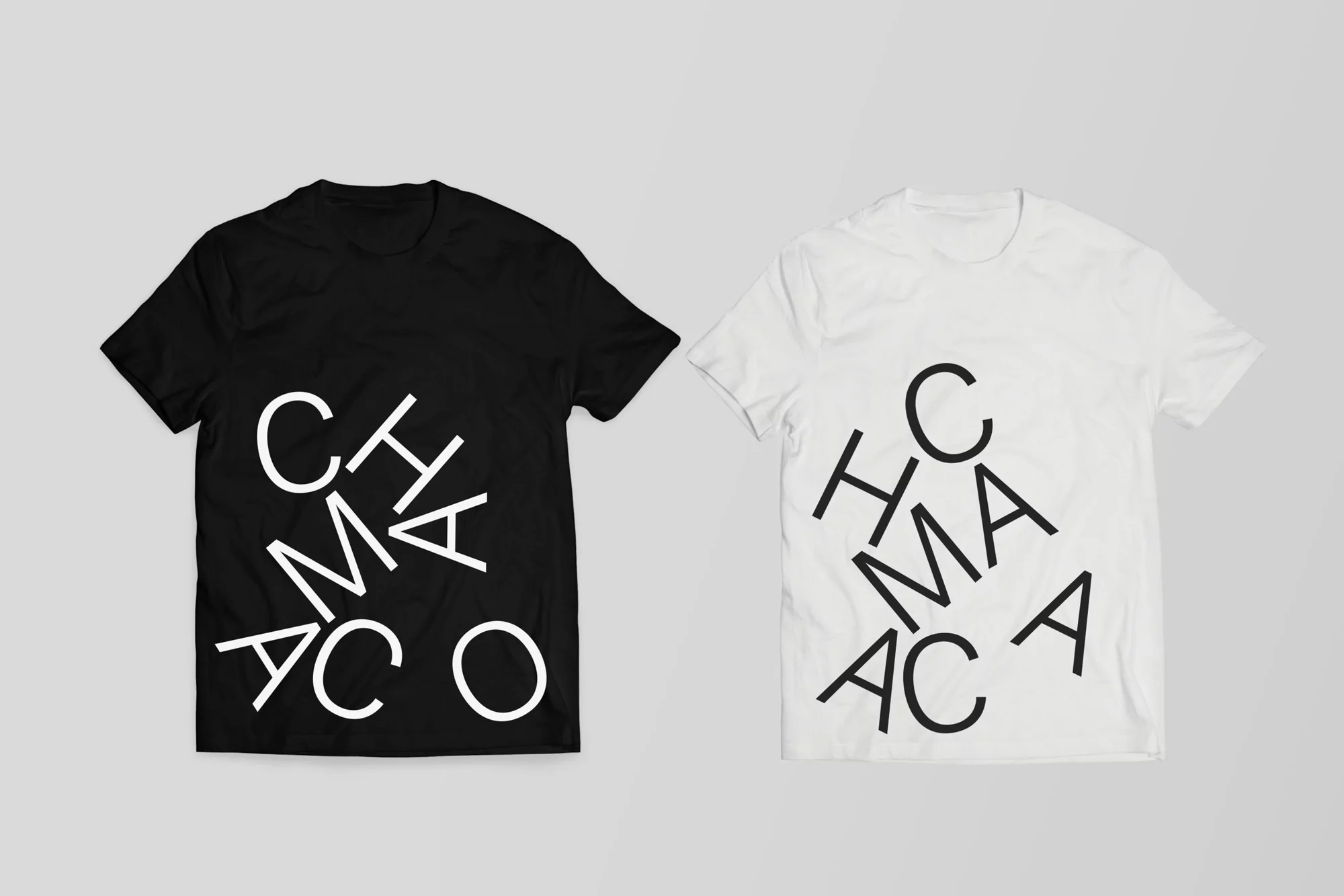 Two t-shirts, one black and one white, display a vertically stacked text design with a casual studio presentation.