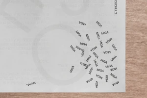 Printed white paper sheet featuring repeated black text MIGA scattered across the surface resting on wooden table