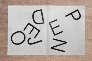 An open printed poster featuring bold black typography set against a light grey paper background resting on a wooden surface.