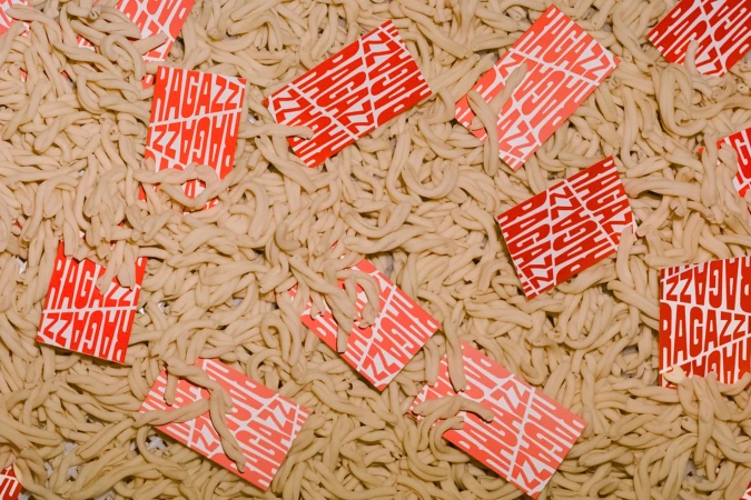 Overhead shot featuring an abundance of fresh pasta alongside several red and white branded cards scattered amongst the noodle piles.