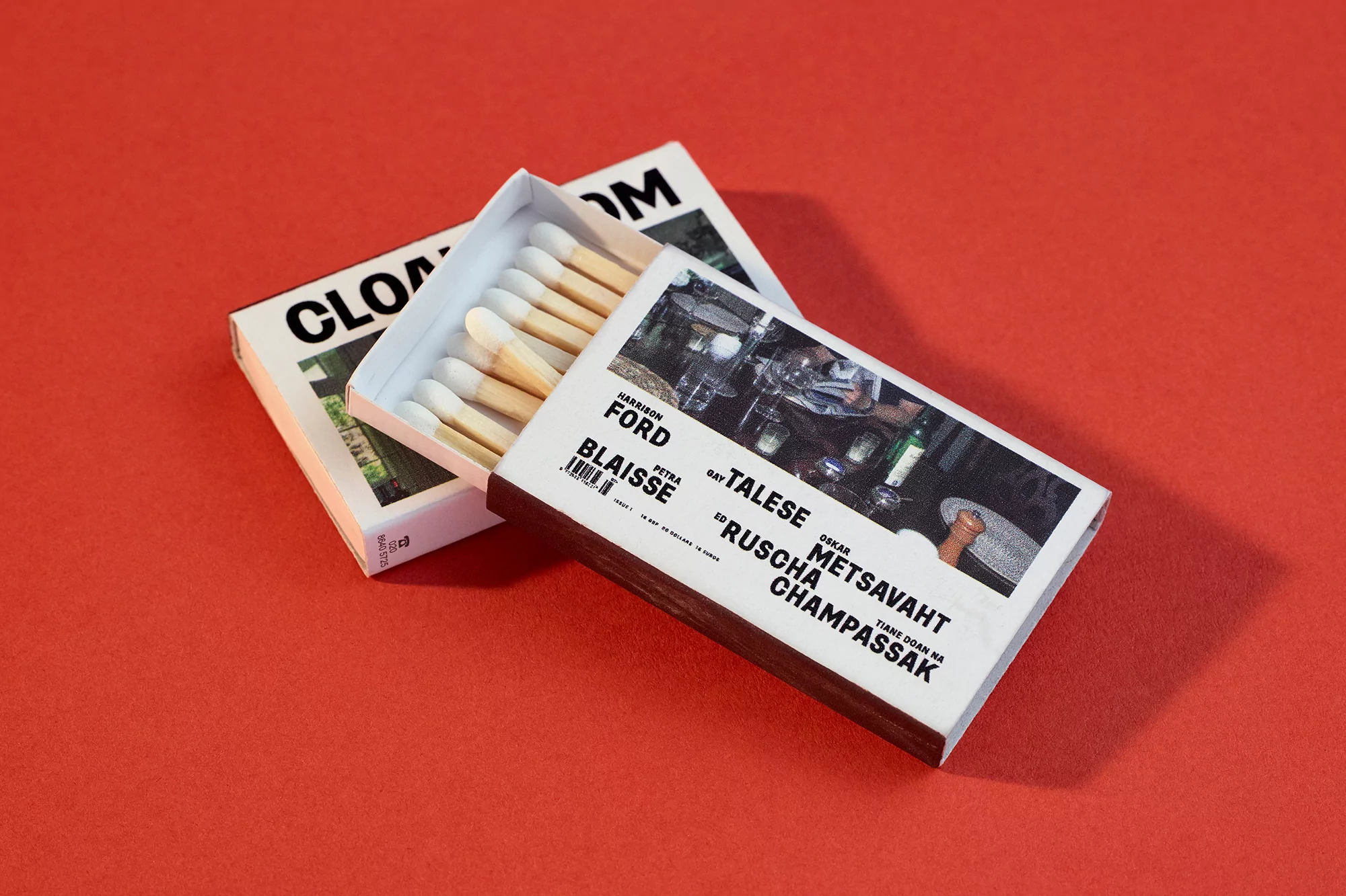 Two matchboxes featuring Cloakroom Magazine branding resting on a solid red background