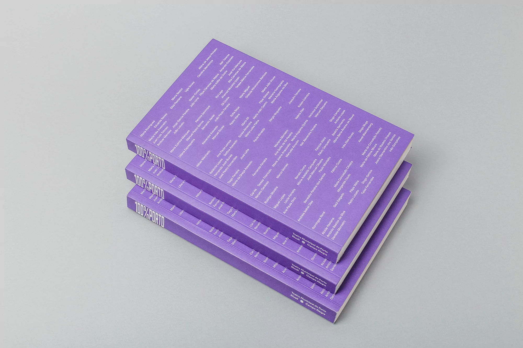 Three violet-covered books are stacked on a light gray surface with visible text titles and author names on the covers and spines.