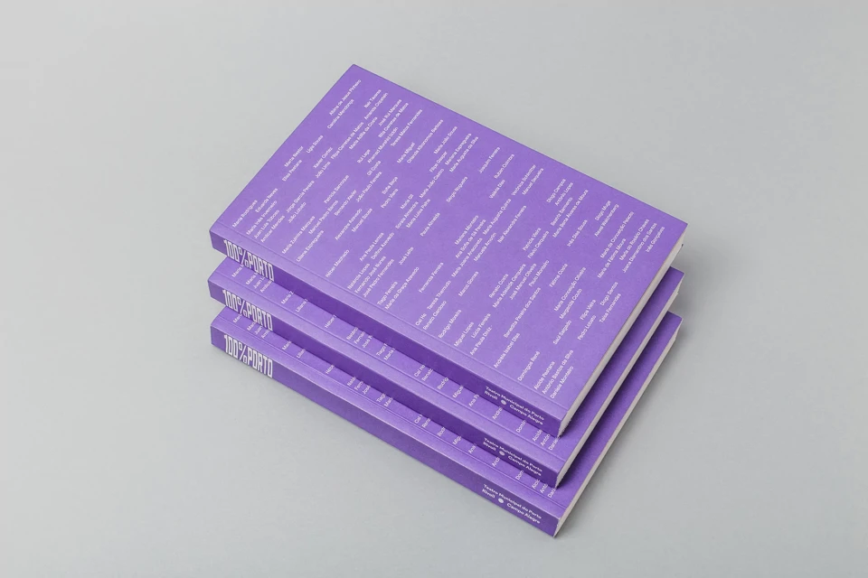 Three violet-covered books are stacked on a light gray surface with visible text titles and author names on the covers and spines.