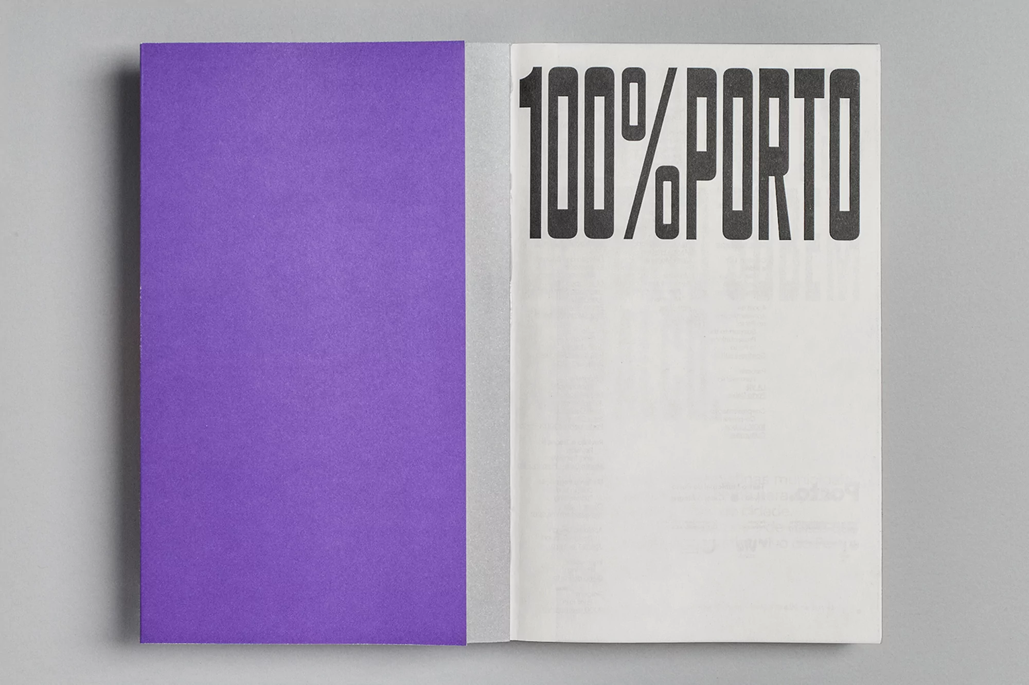 Open book with one purple page and the other with bold black text '100% PORTO' on a gray surface, creating a minimalistic design.
