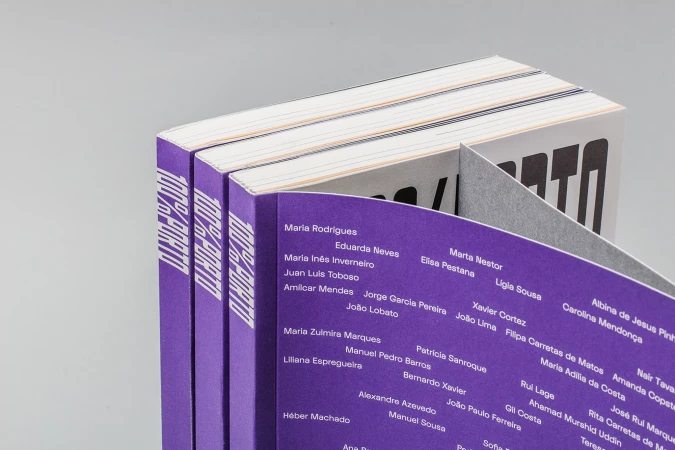 Stack of purple books with visible text "100% Porto" and a list of names, close-up shot, studio lighting. Books appear to be newly published.