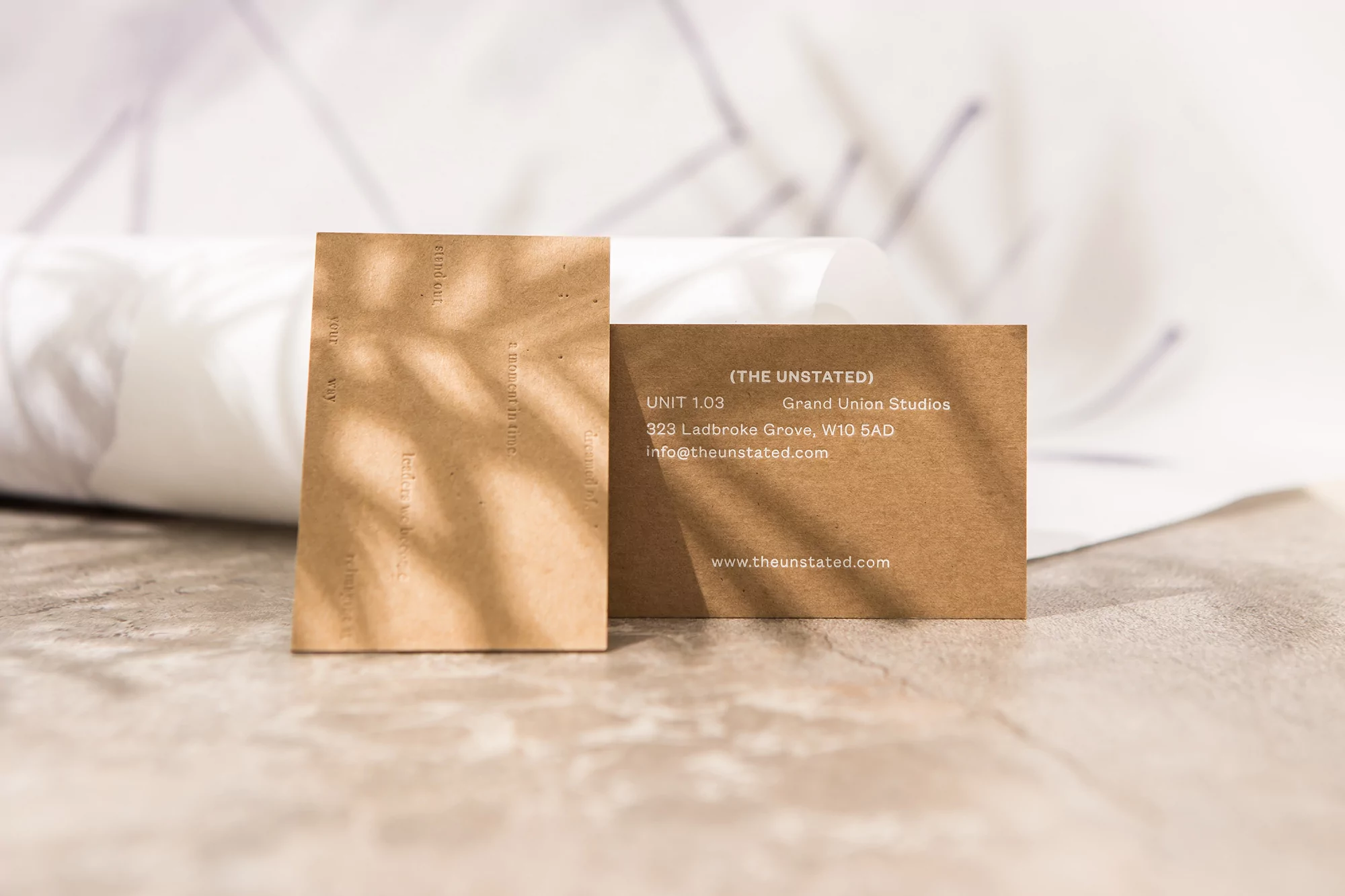Two kraft paper business cards with address, studio name, and website displayed against a gray surface with a soft white background.