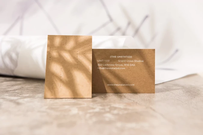 Two kraft paper business cards with address, studio name, and website displayed against a gray surface with a soft white background.