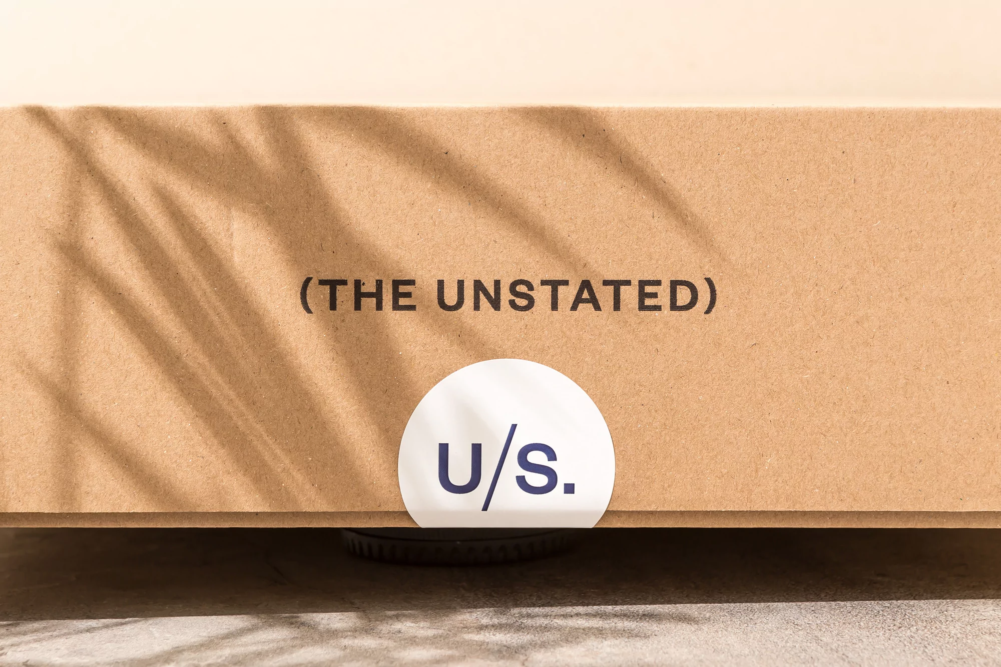 Close-up of a cardboard box with the brand name THE UNSTATED printed on it and a circular sticker with U/S in dark blue.