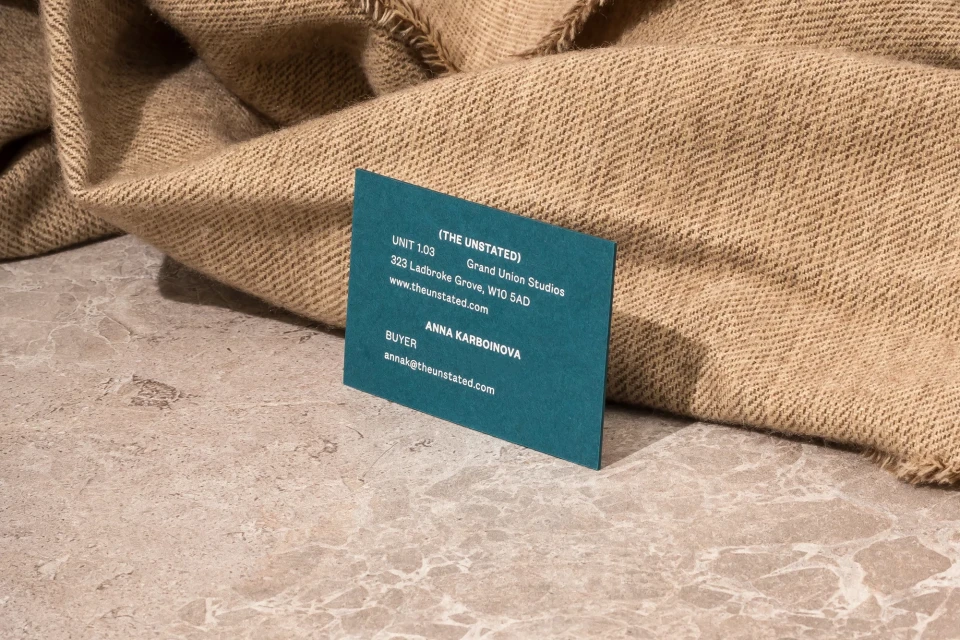 Close-up of a blue business card resting on a stone surface, with a beige, textured fabric draped in the background.
