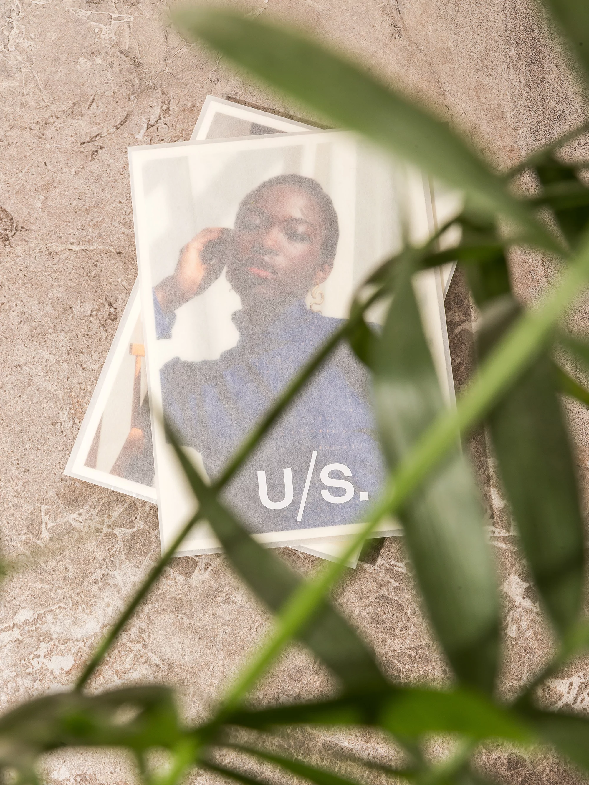 A stack of fashion magazine covers features an elegant Black woman in a navy top, set against a gray marble background and green plant.