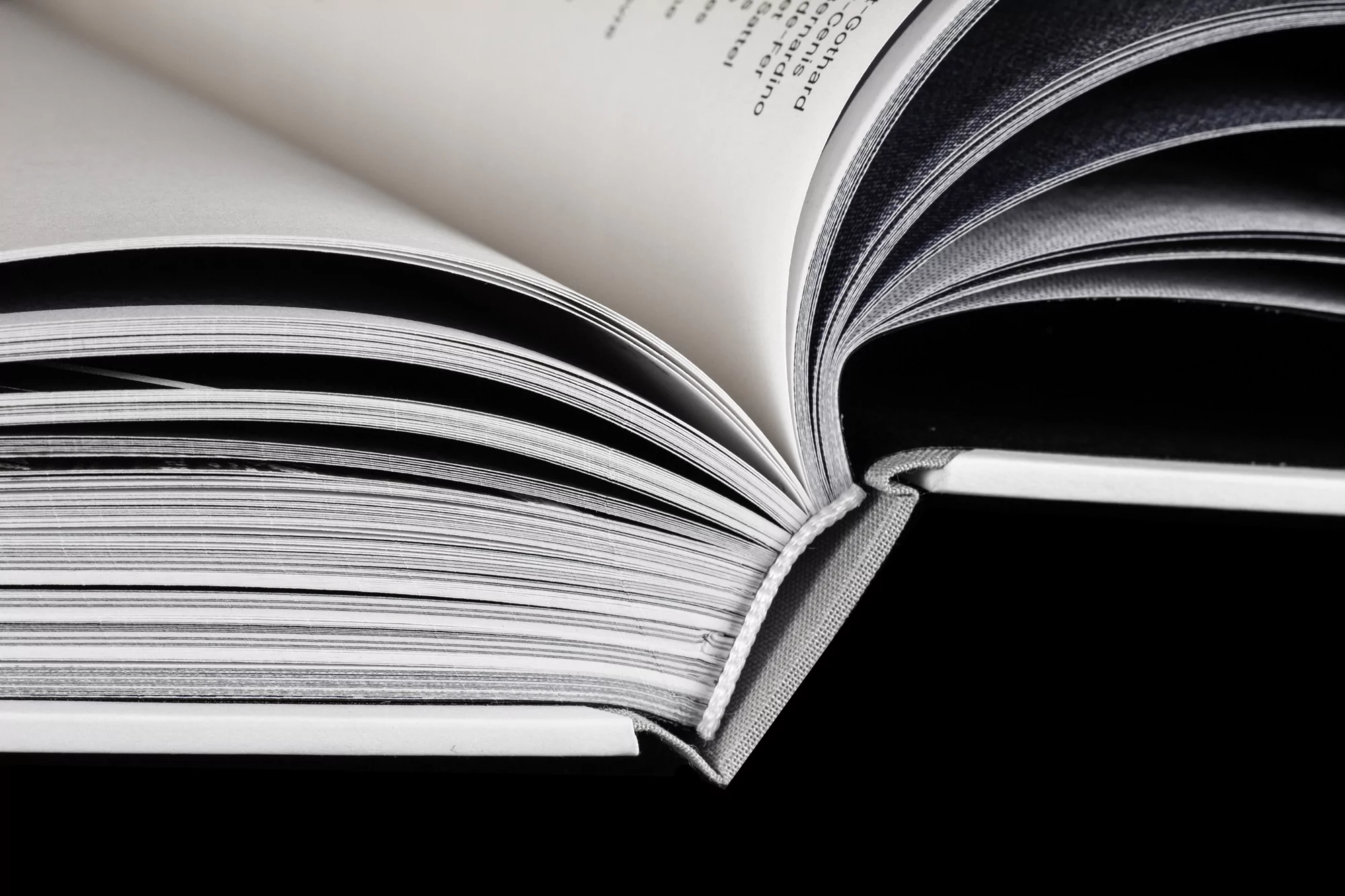 Open book with white pages and gray binding on a black background, showcasing depth of field and contrasting colors, suitable for educational use.