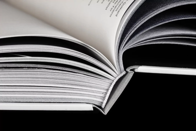 Open book with white pages and gray binding on a black background, showcasing depth of field and contrasting colors, suitable for educational use.