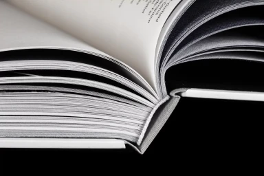 Close-up macro shot of an open hardcover book showing stacked paper pages and binding against a dark background