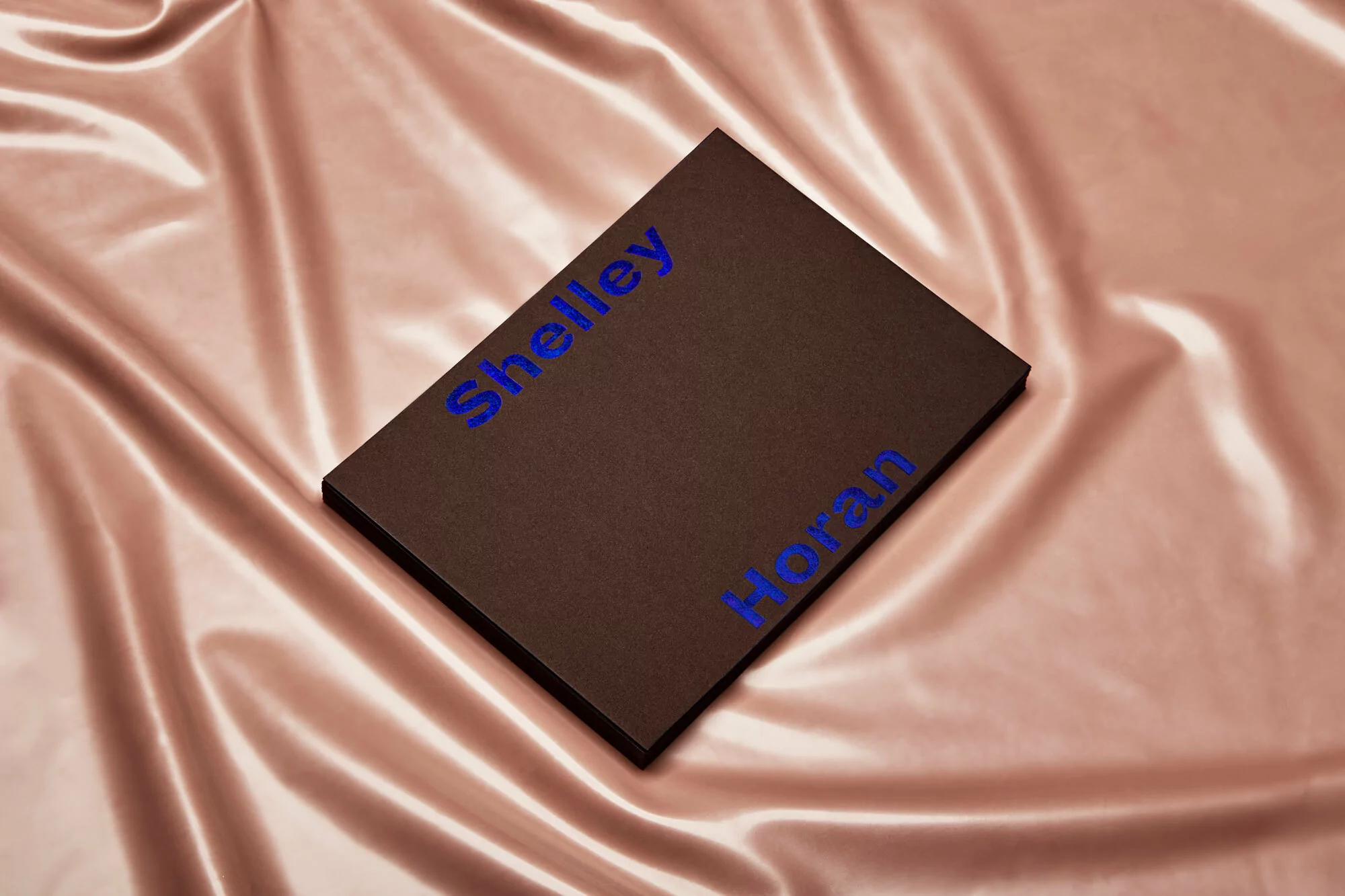 Dark brown book with blue text on a wrinkled light pink satin fabric background creating a visually appealing contrast.