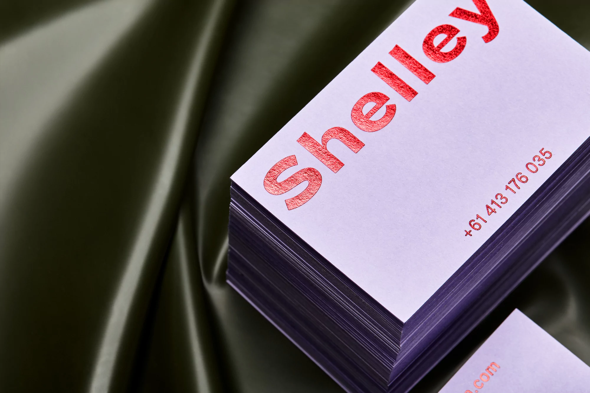 Stack of white business cards with red text on green satin fabric background in a close-up studio shot for marketing and design.