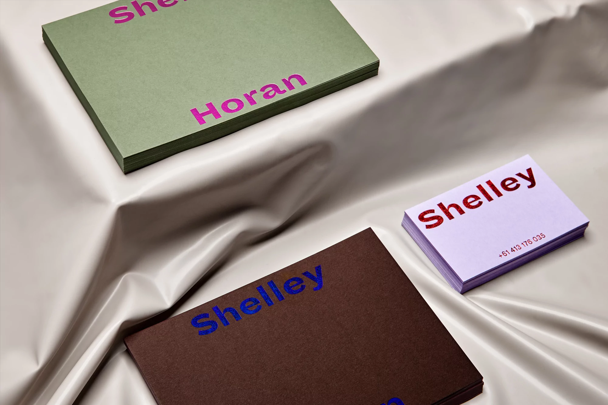 Stacks of business cards in brown, green, and purple with text in bright pink, blue, and red, placed on a draped surface.