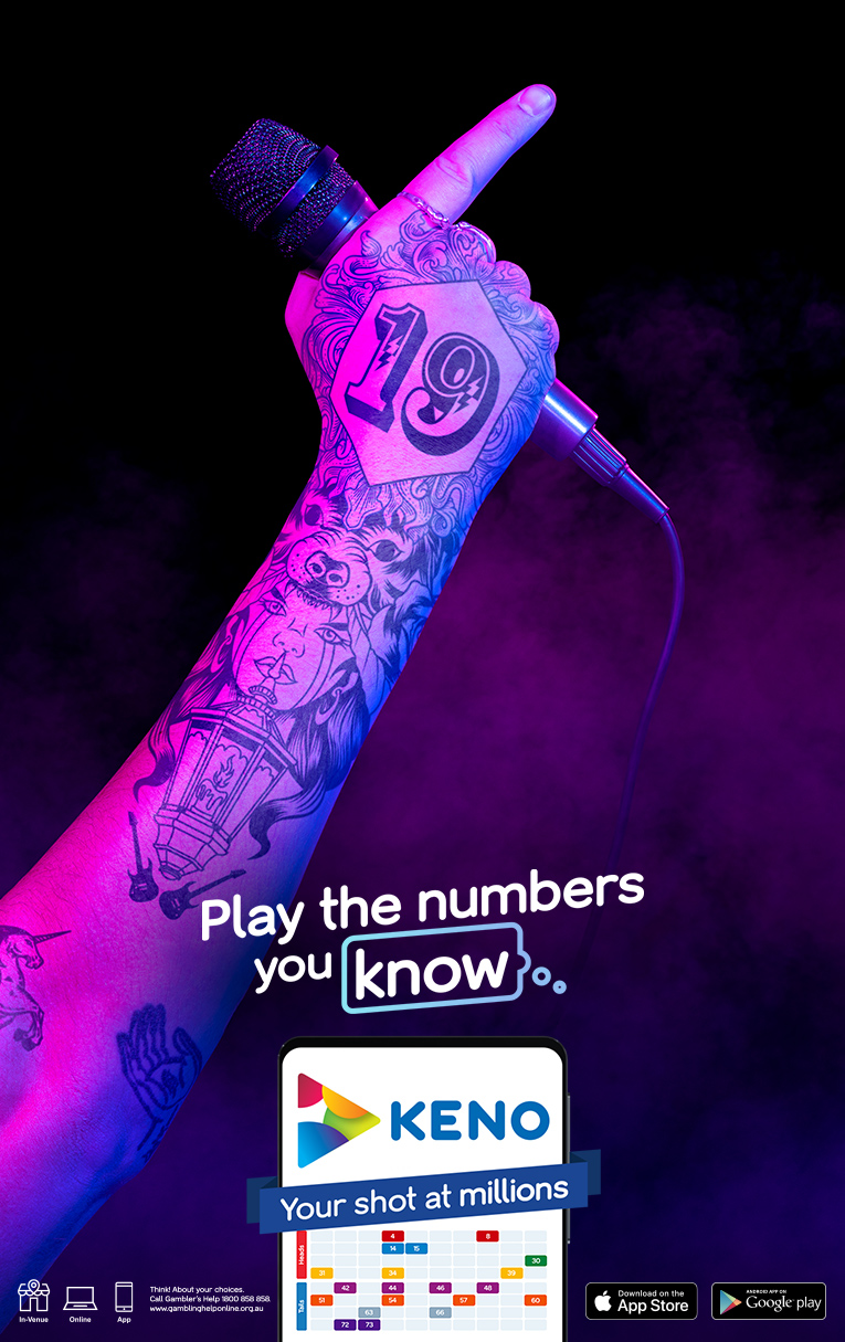 Close-up of a tattooed hand holding a microphone against a dark backdrop with an advertisement for a Keno game on a mobile phone.