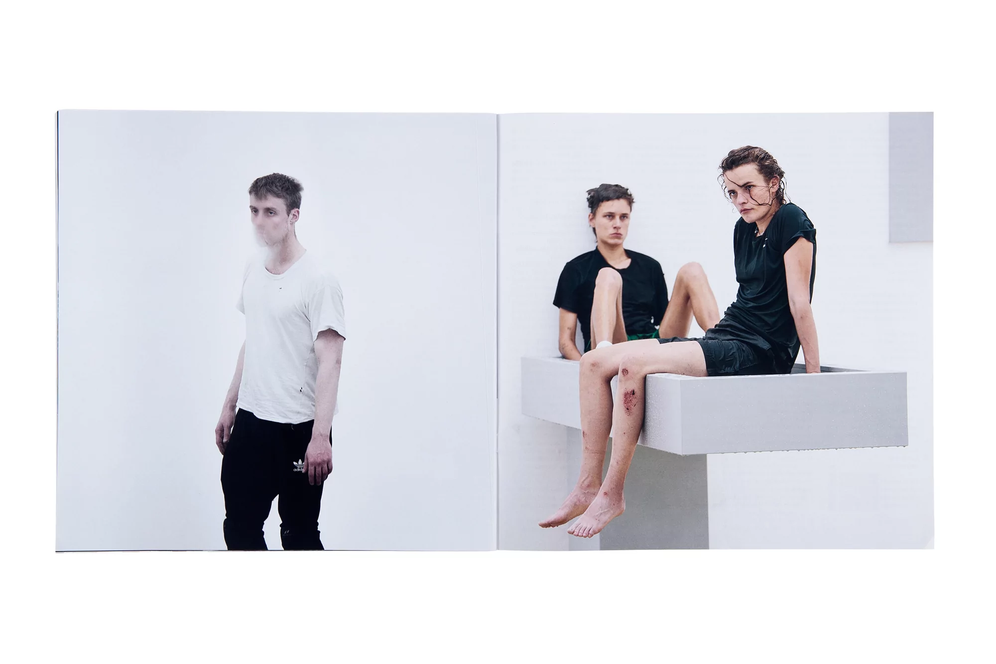 Two young adult women sitting on a white structure, and one young adult male standing next to them, all in a white studio.