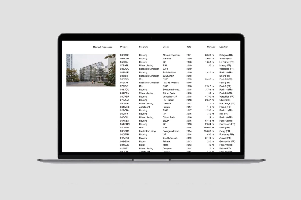 Laptop displaying a table with architecture project data, including project names, dates, surface areas, and locations against gray backdrop.