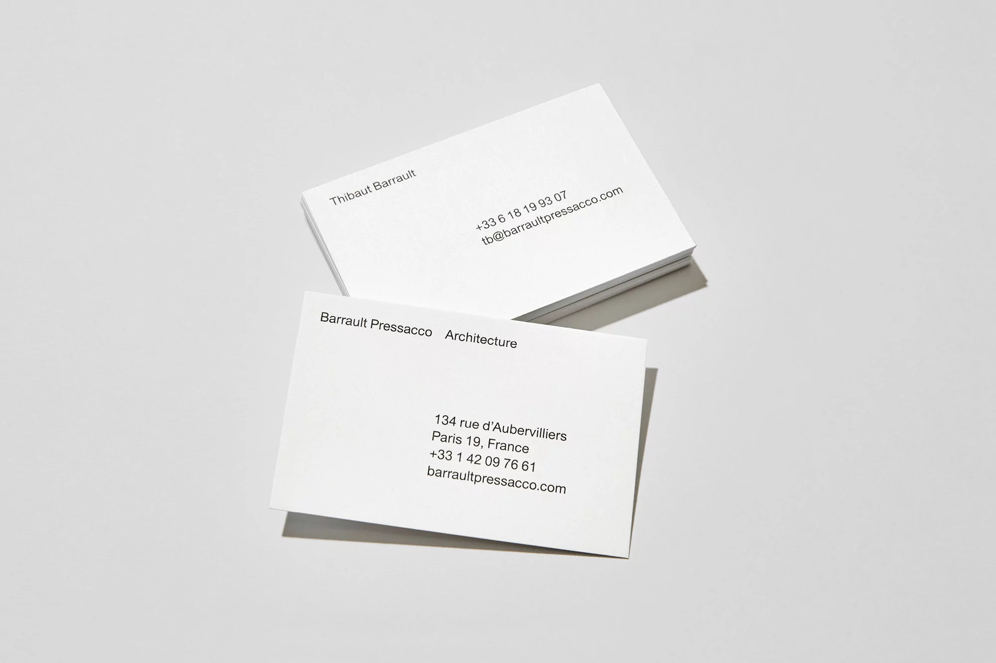 Two stacks of white business cards featuring company and contact information on a white surface in minimalist style.