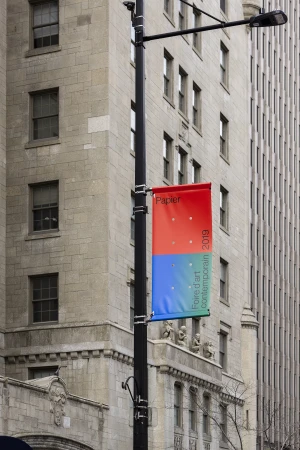 Cityscape featuring a lamp post displaying an art fair banner for Papier 2019, with the backdrop of vintage architecture.