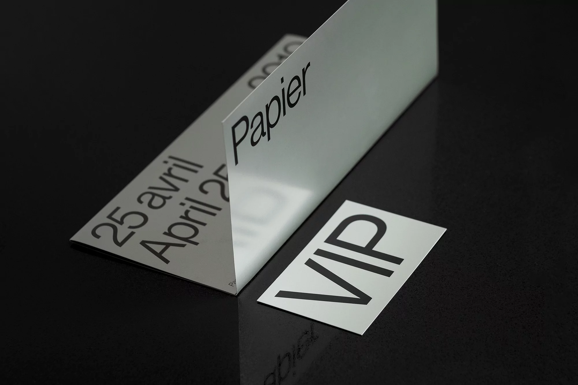 Close-up of a crisp white 'Papier' invitation card on a glossy black surface, highlighting its simple typography and elegant design.