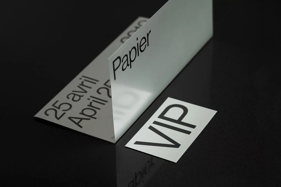 Close-up of a crisp white 'Papier' invitation card on a glossy black surface, highlighting its simple typography and elegant design.